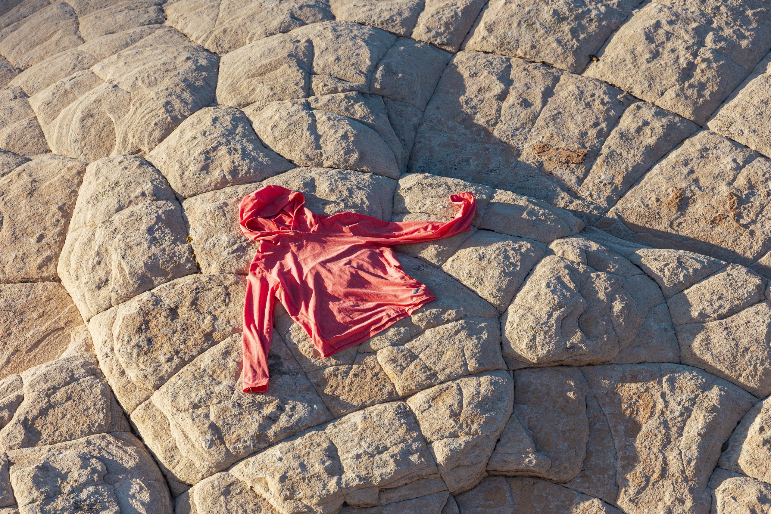A red sun hoodie is laid out flat on a rock in direct sunlight