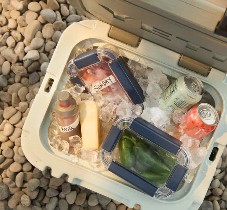Picture of a cooler filled with ice, canned drinks and food. 