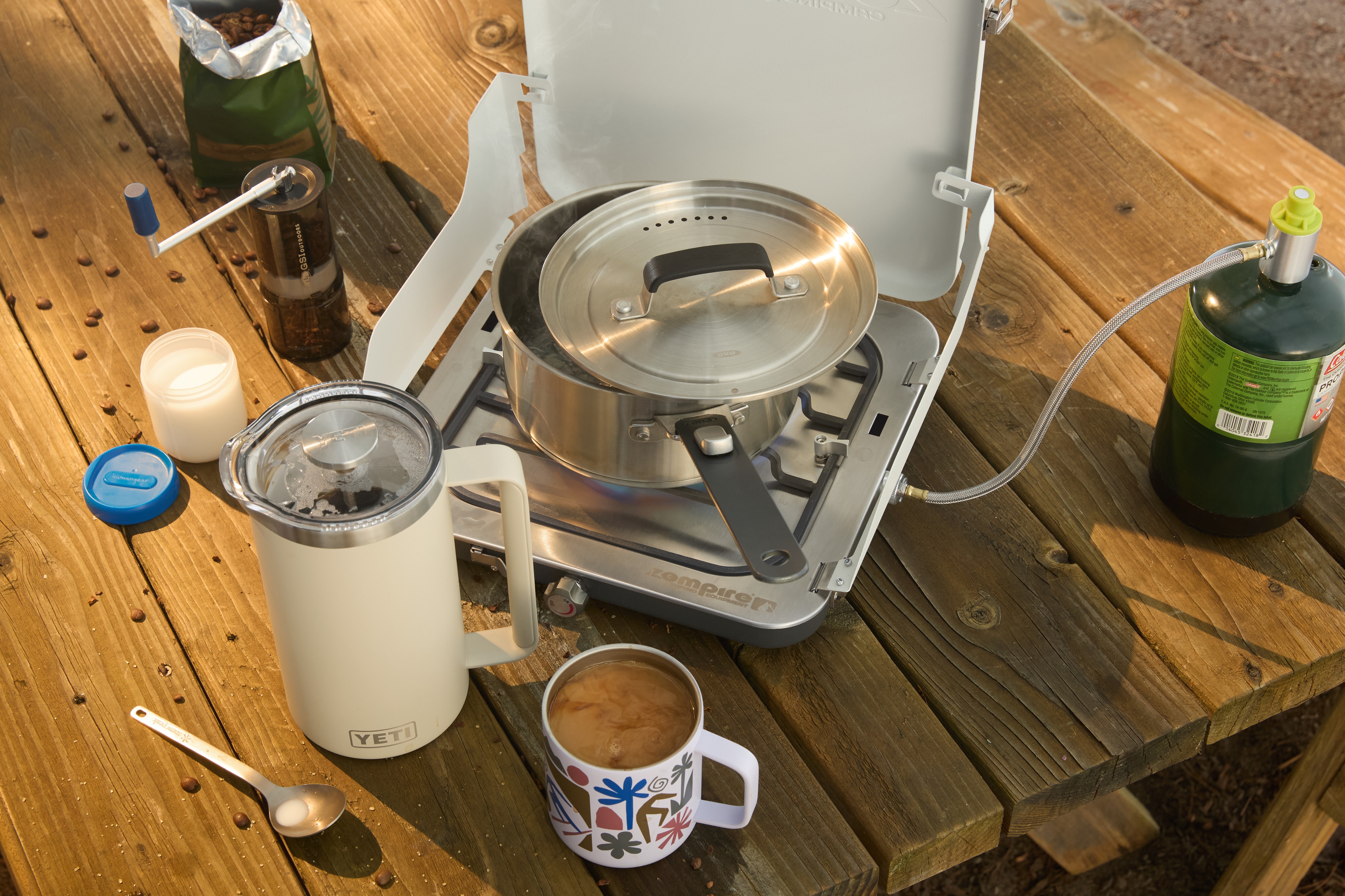 A Zempire stove, YETI French press, insulated mug, & utensils on a table.