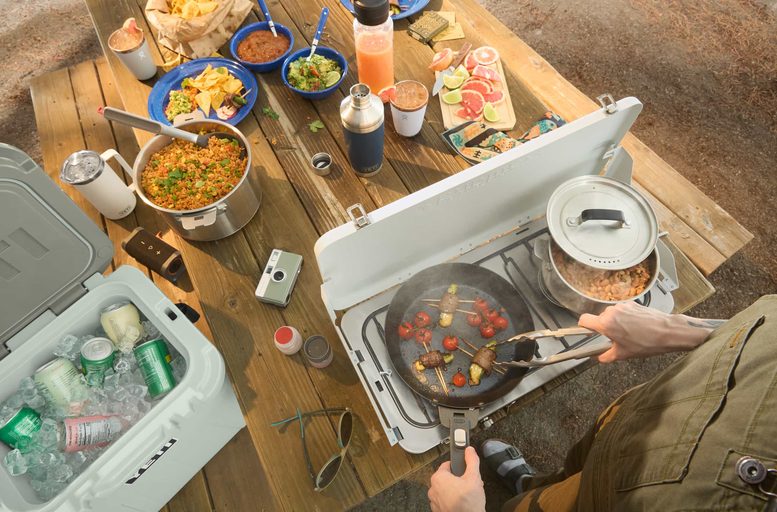 Picture of person cooking on camp stove at a campground table.