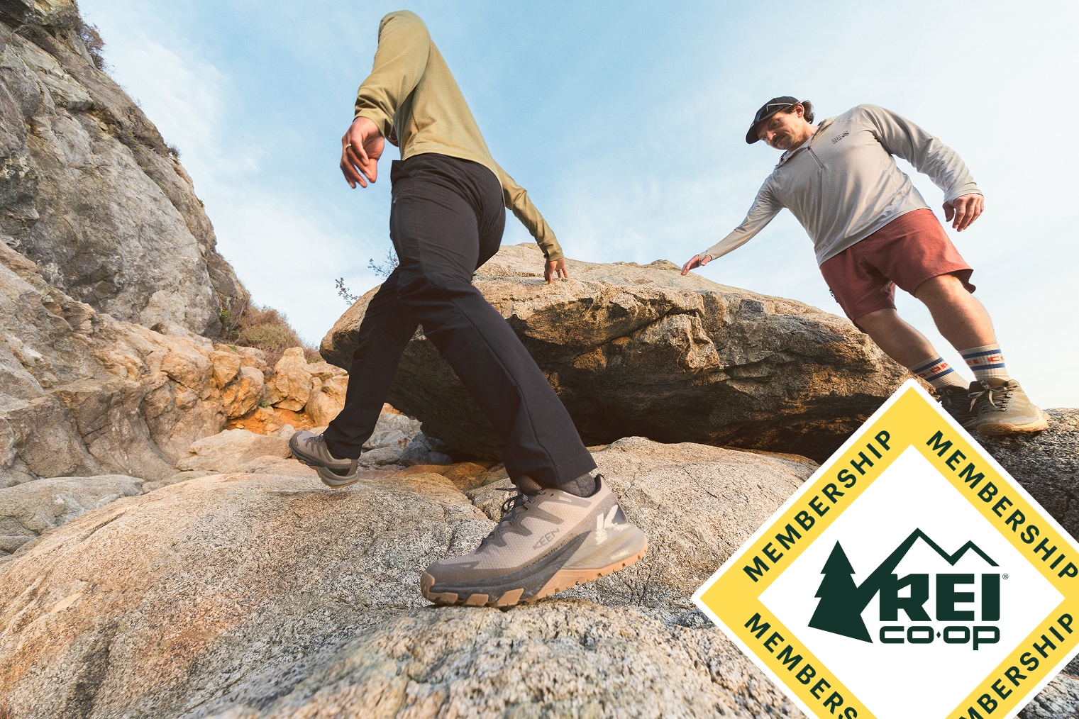 Two friends scramble on a rocky outcrop under blue skies and fluffy clouds.