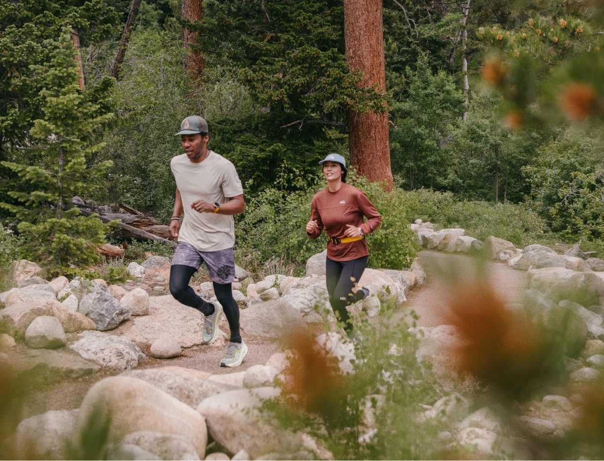 Two people run through a trail lined with rocks and trees.