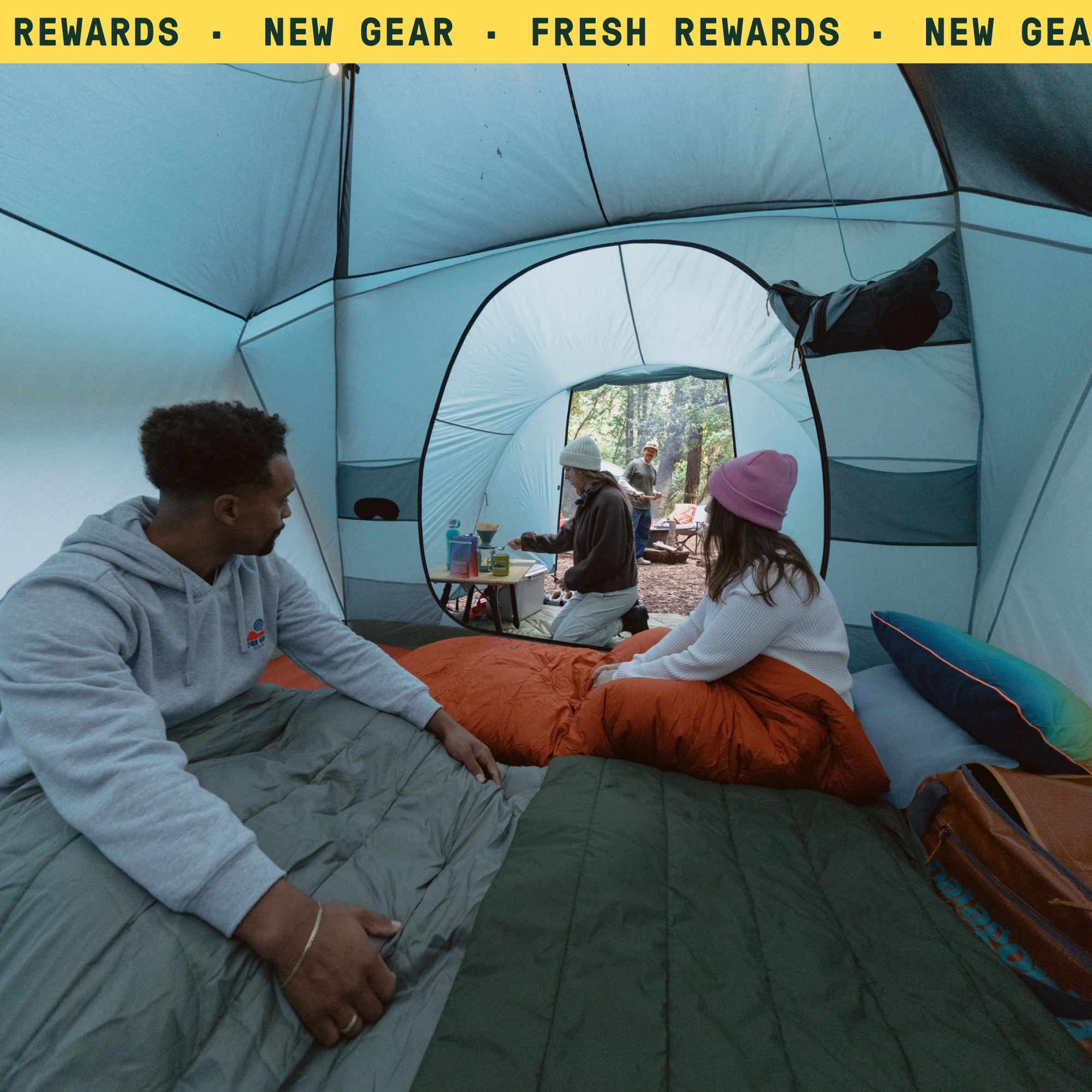 A person makes coffee while two people relax inside of a tent.