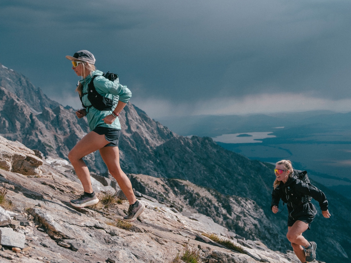 Two people run up a large rock together.