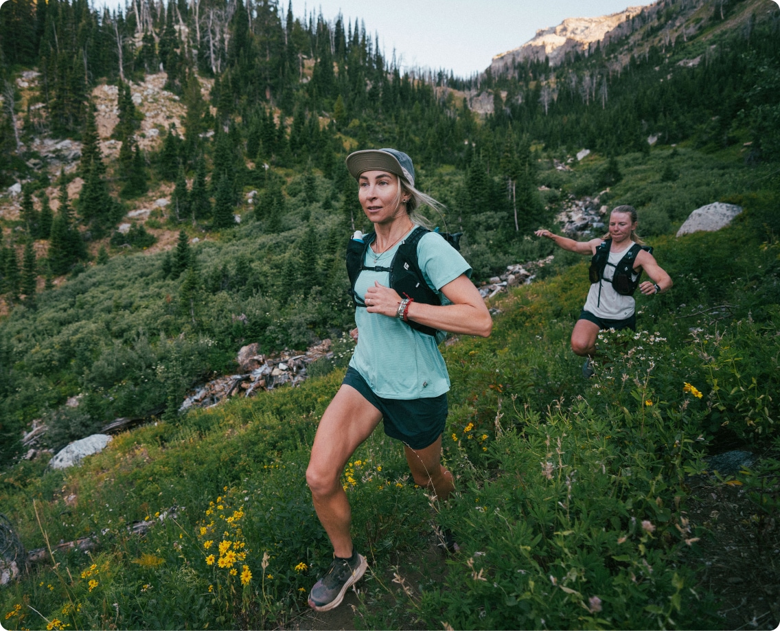 Two people run together through a grass lined trail.