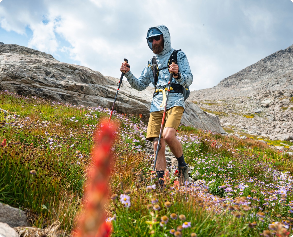 A person hikes through a grassy hillside with their trekking poles.