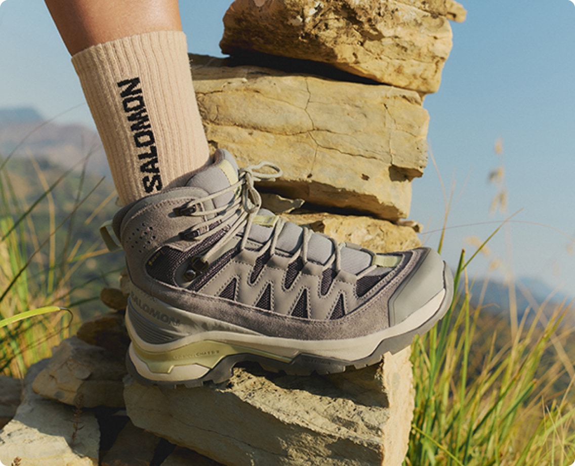 A person rests their foot on a stack of rocks while wearing Salomon socks and hiking shoes.