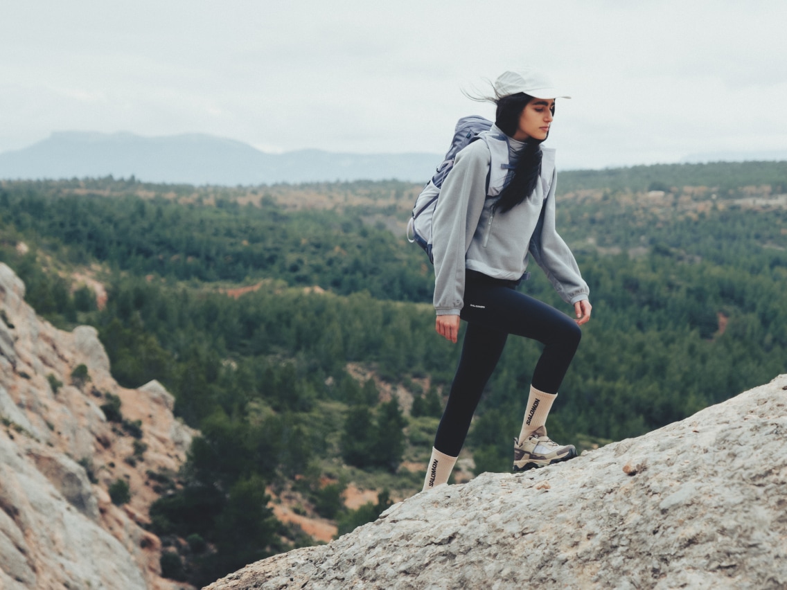 A person hikes up a large rock on a windy day.