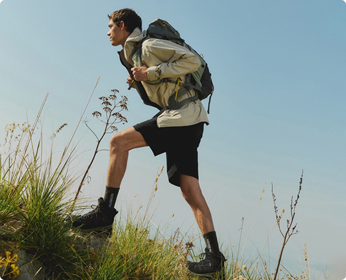 A person hikes up a grassy hill in their Salomon gear on a sunny day.