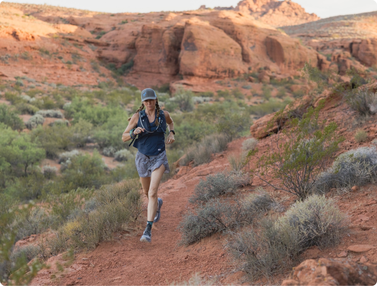 A person wearing a hydration pack runs through a desert trail.