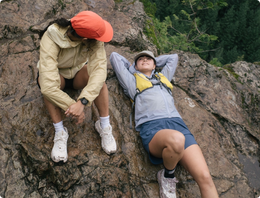 Two people relax on a rock in their running gear.