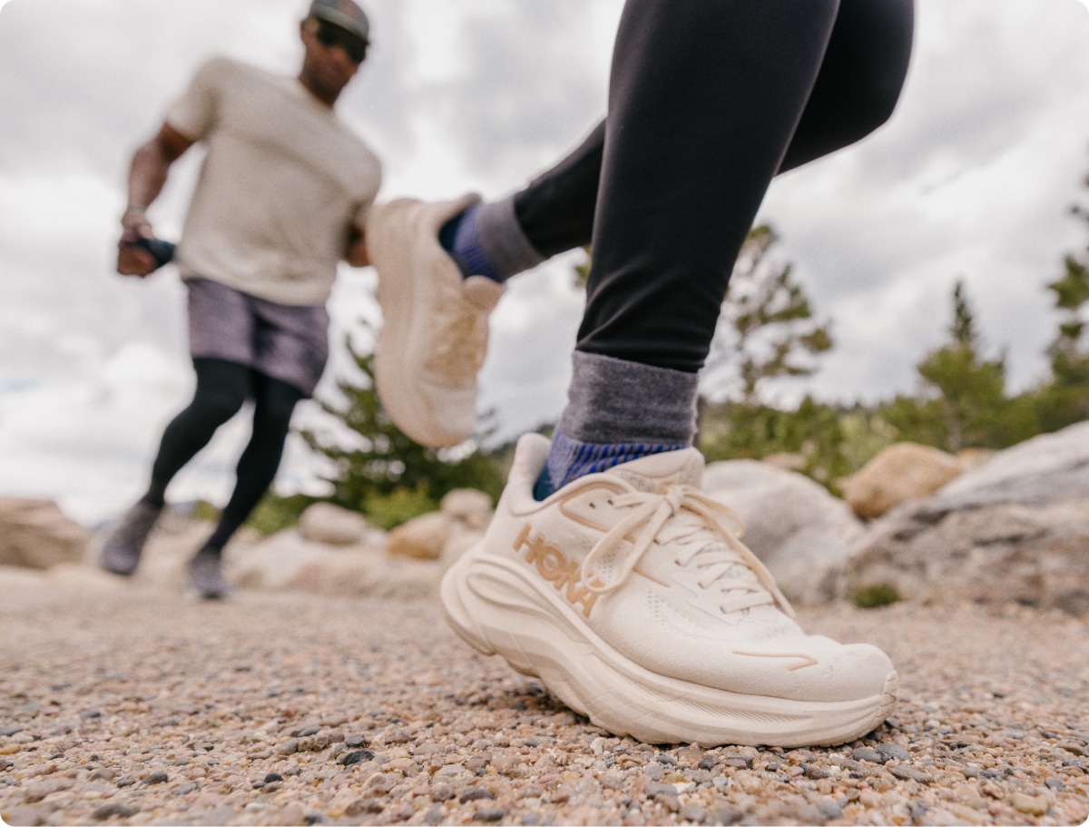 Two people run through a gravel path on a sunny day.