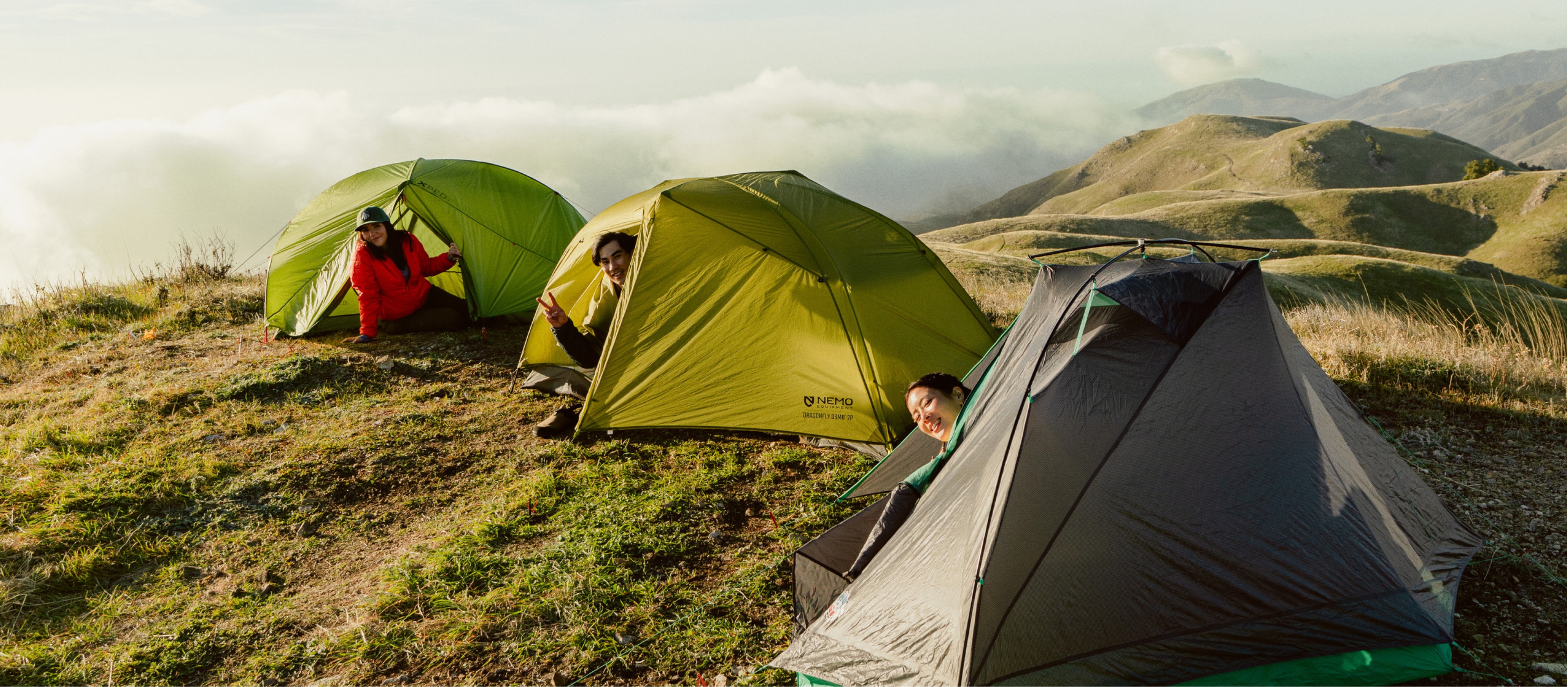 Three people stick their heads outside of their tents while smiling for the camera.