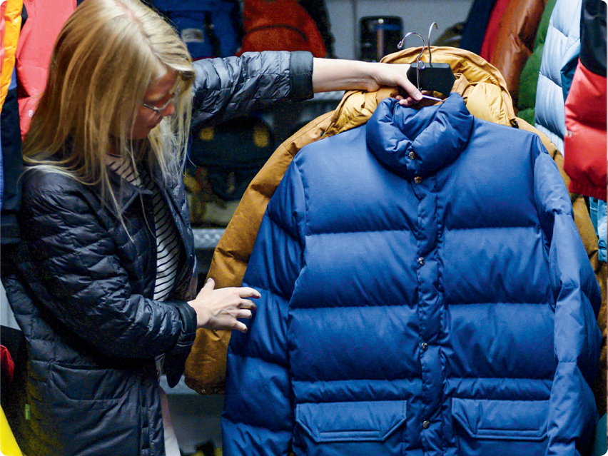 A person holding two puffer jackets on hangers.