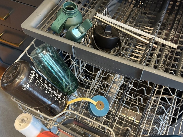 Several water bottles are placed in a dishwasher for cleaning.
