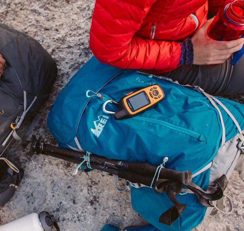 A backpacker sits down next to their pack and drinks from their water bottle.