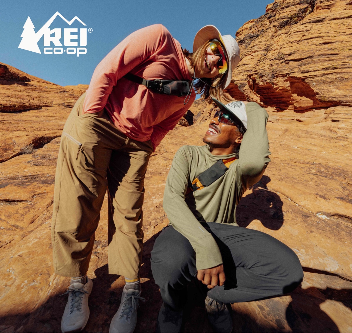 Two hikers laugh and smile for the camera while wearing clothing from the R E I Co-op Trailmade Collection.