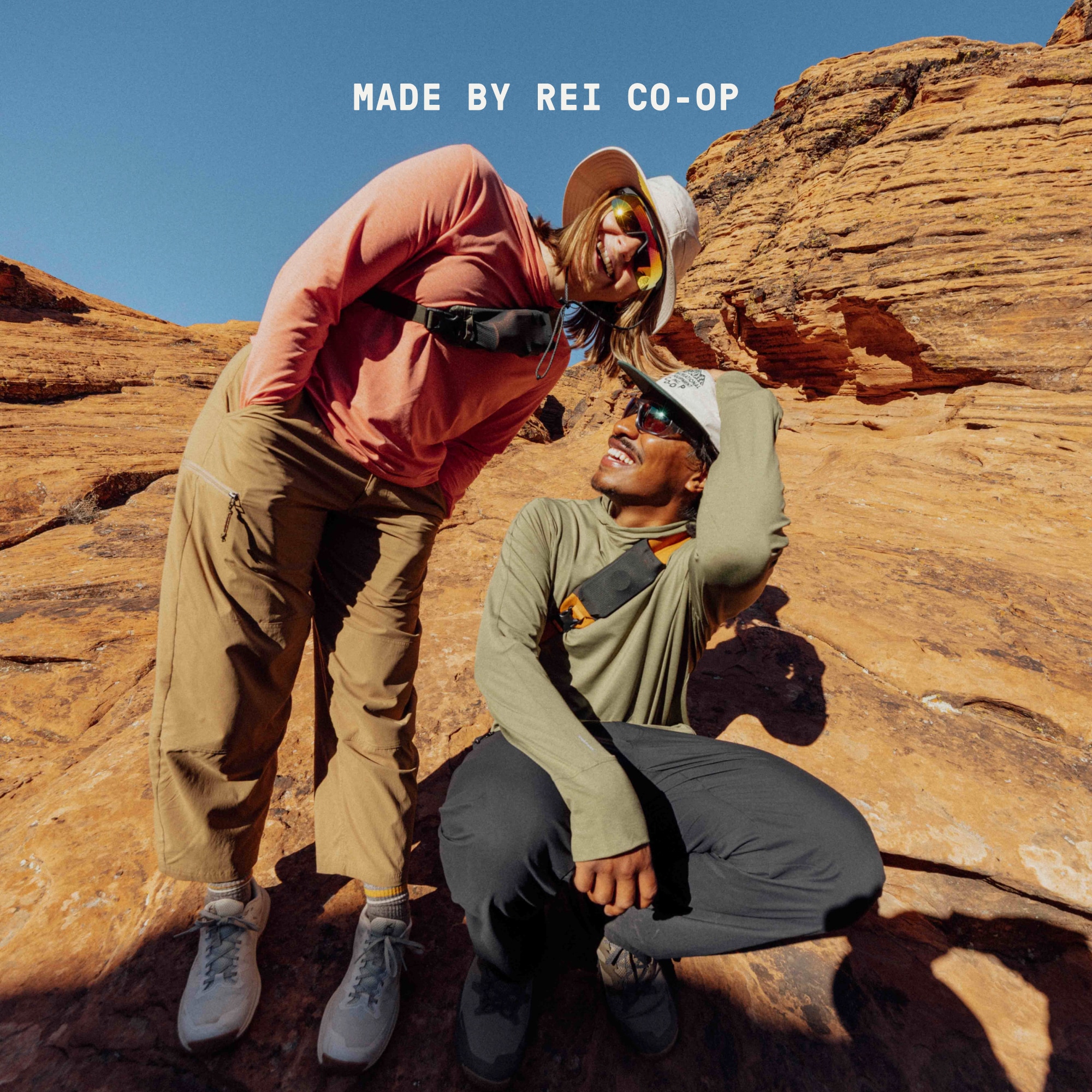 Text reads: ‘Made by R E I Co-op’ over two hikers laughing and smiling for the camera while wearing clothing from the Trailmade Collection.