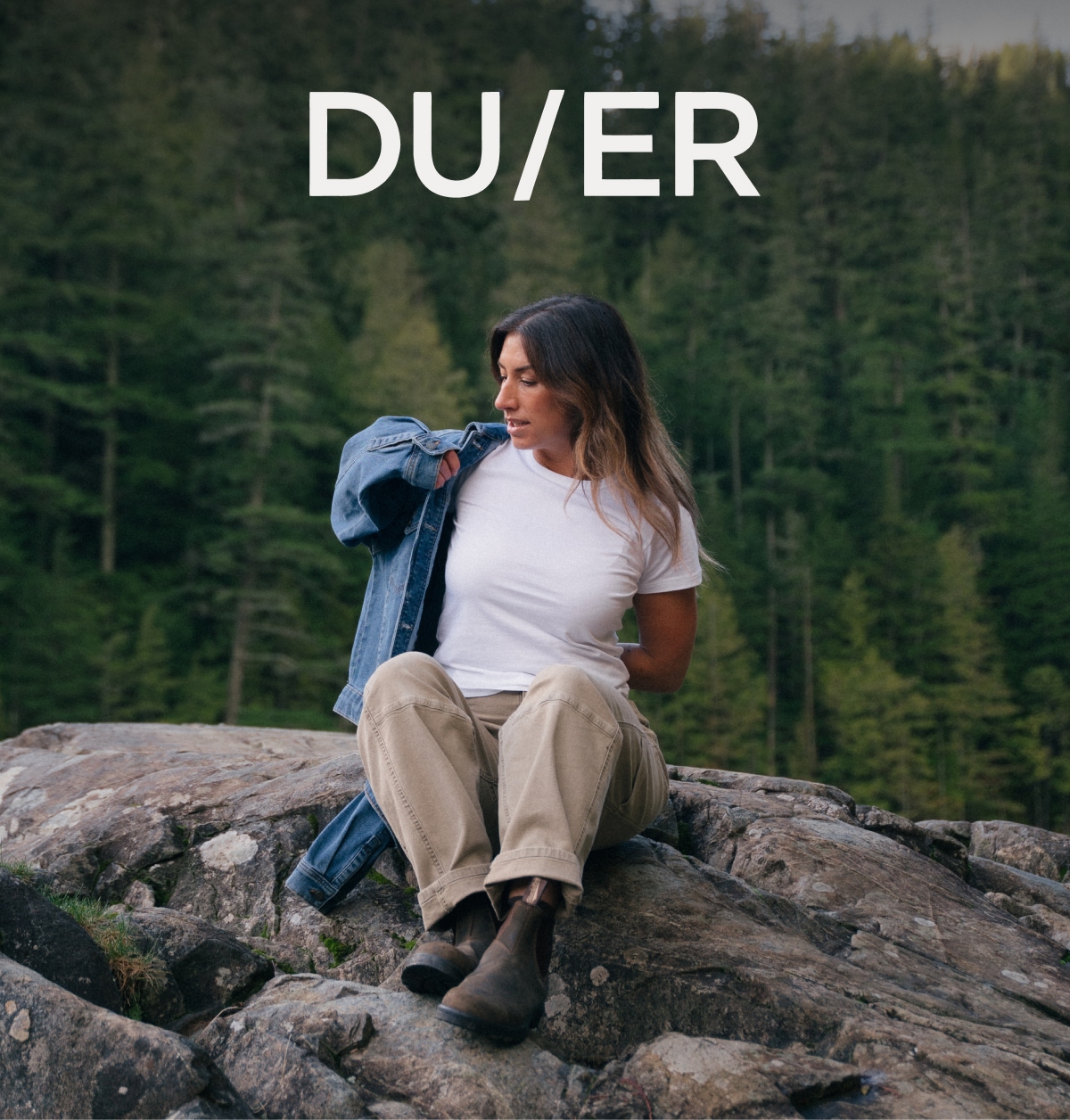 A person sits on top of a large rock in their DUER clothing.