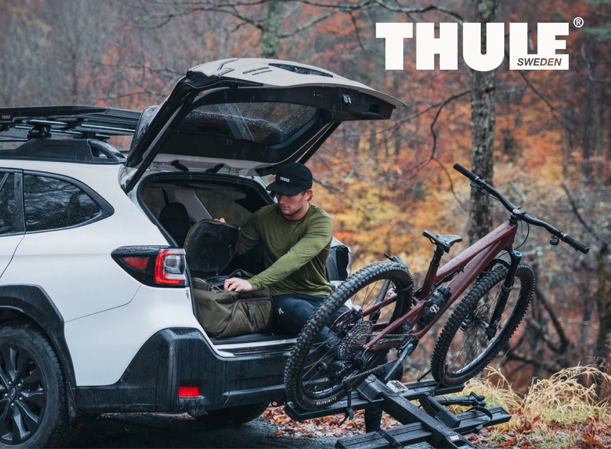 A person sits in the trunk of their car with a bike attached to a Thule rack.