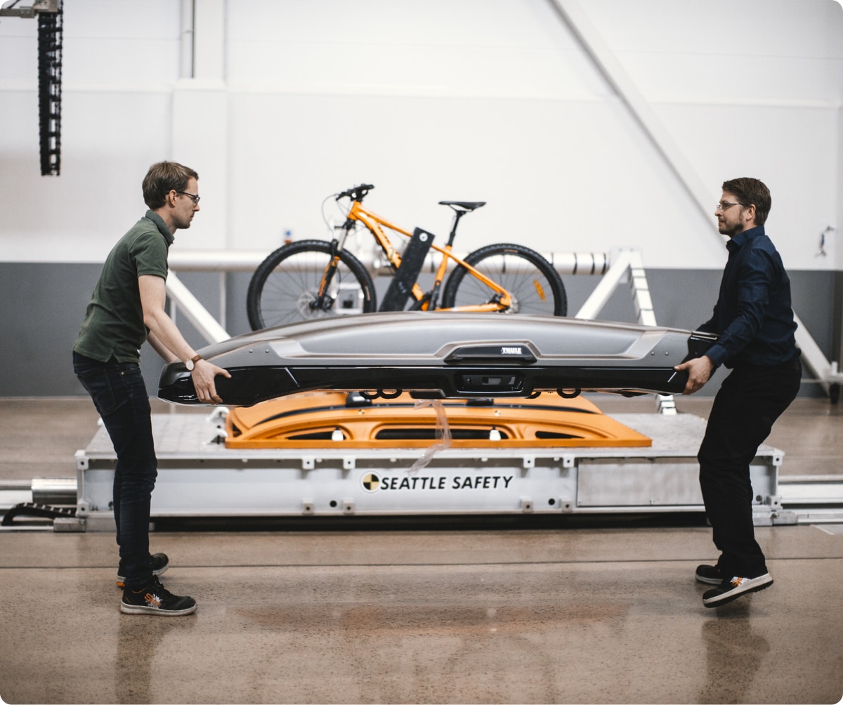 Two people carefully carrying a Thule roof box.