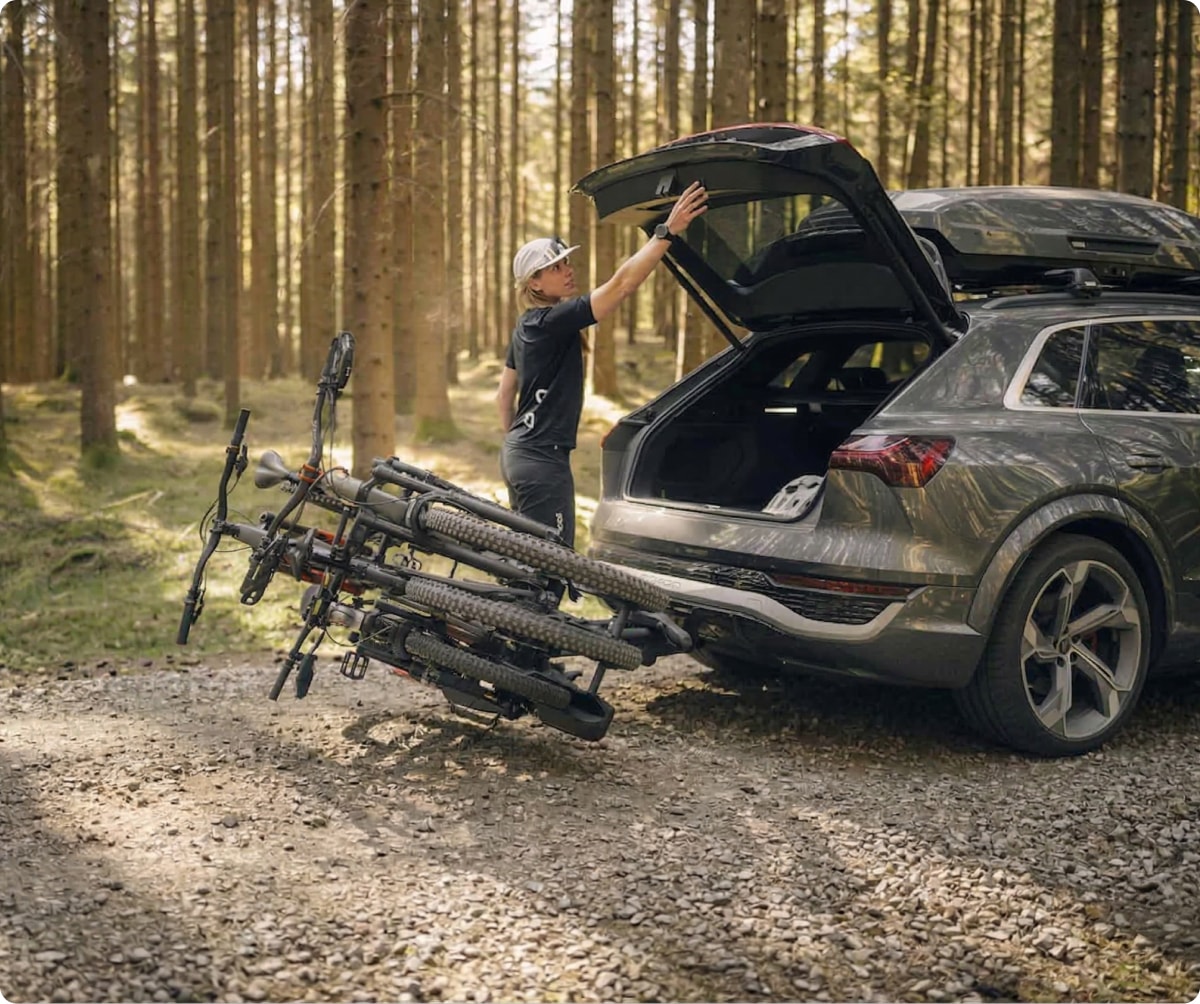 A person closes the trunk to their car with two bikes attached to a rack.