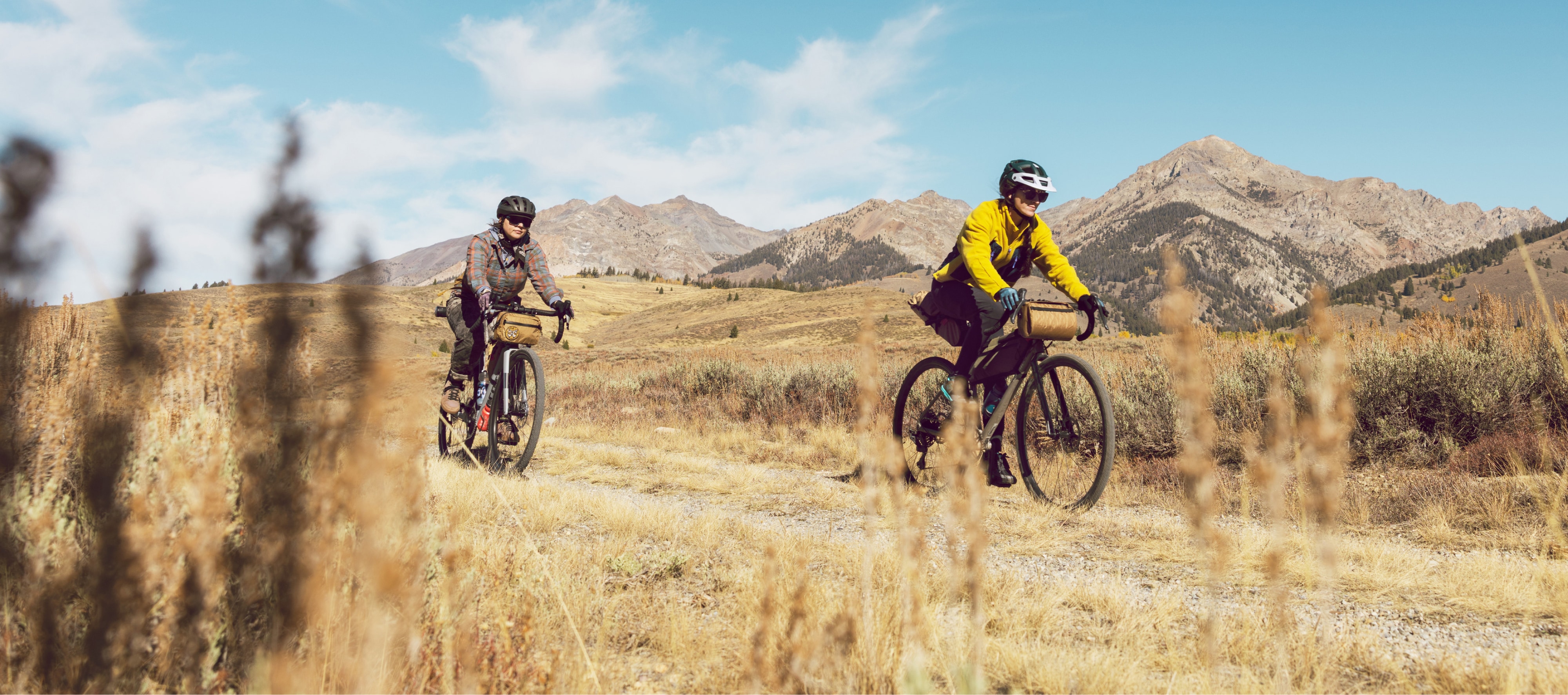 Two people ride bikes through a gravel path on a sunny day.