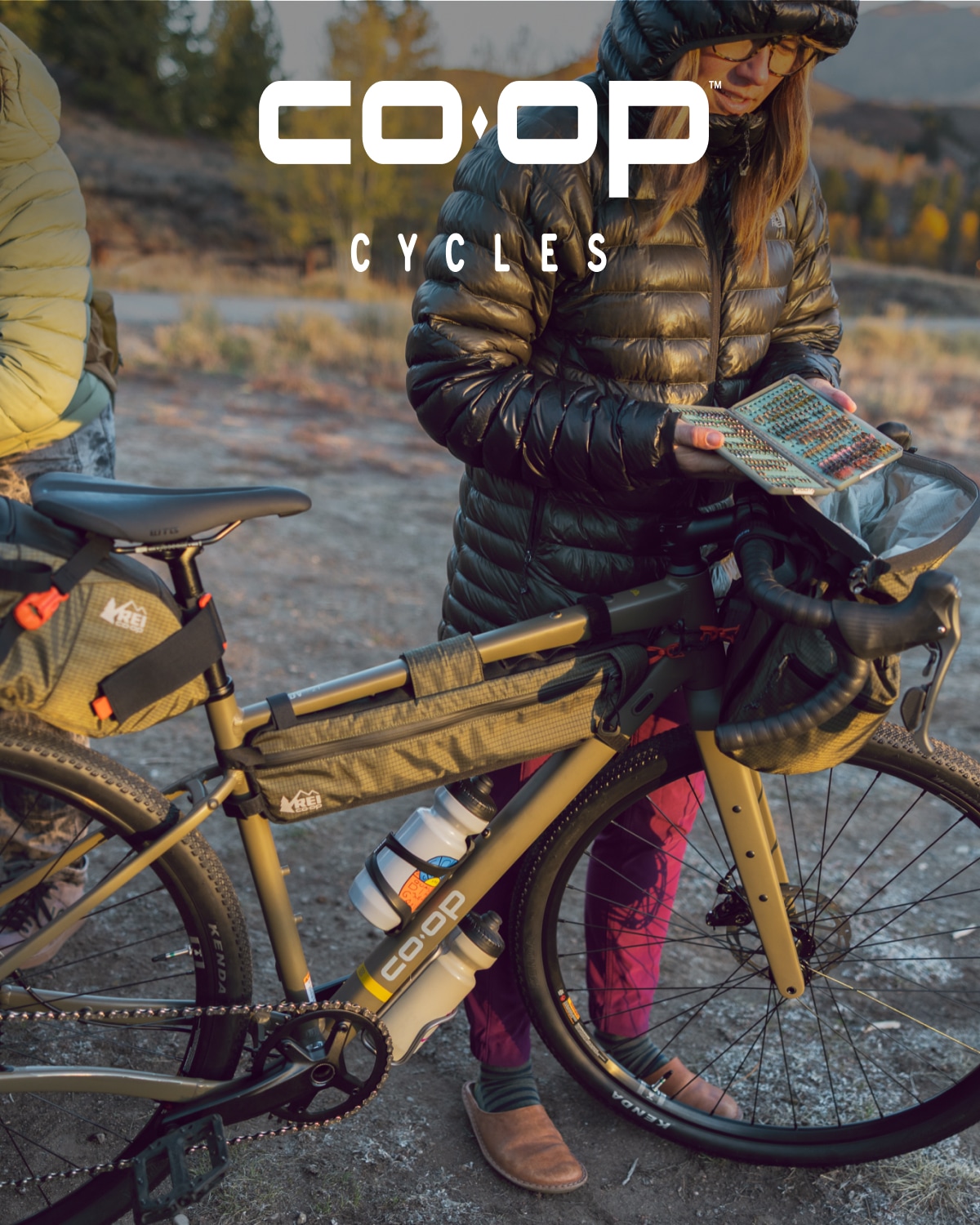 A person stands with their Co-op Cycles bike while they check their gear.