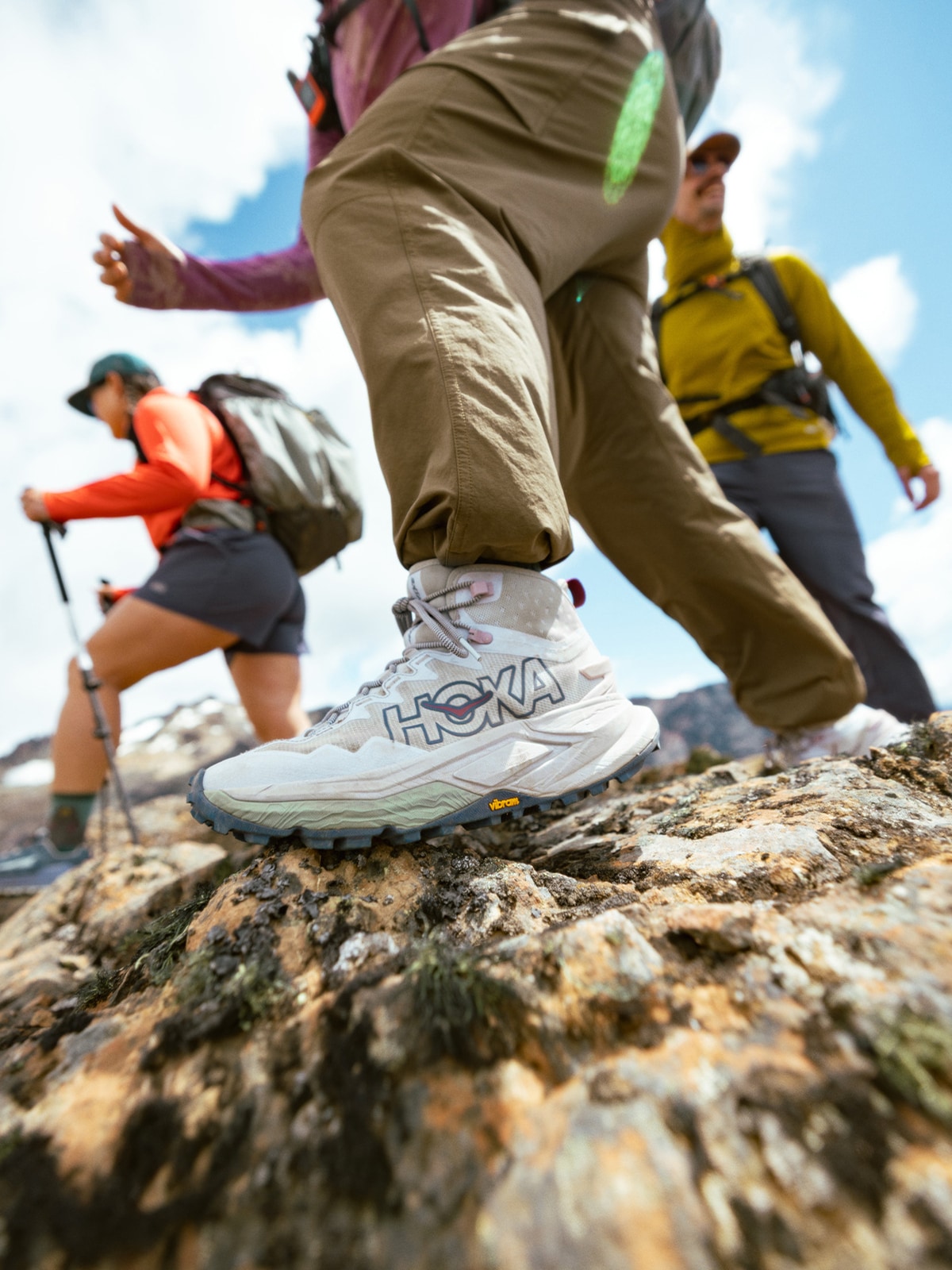 Three people hike over large rocks together.