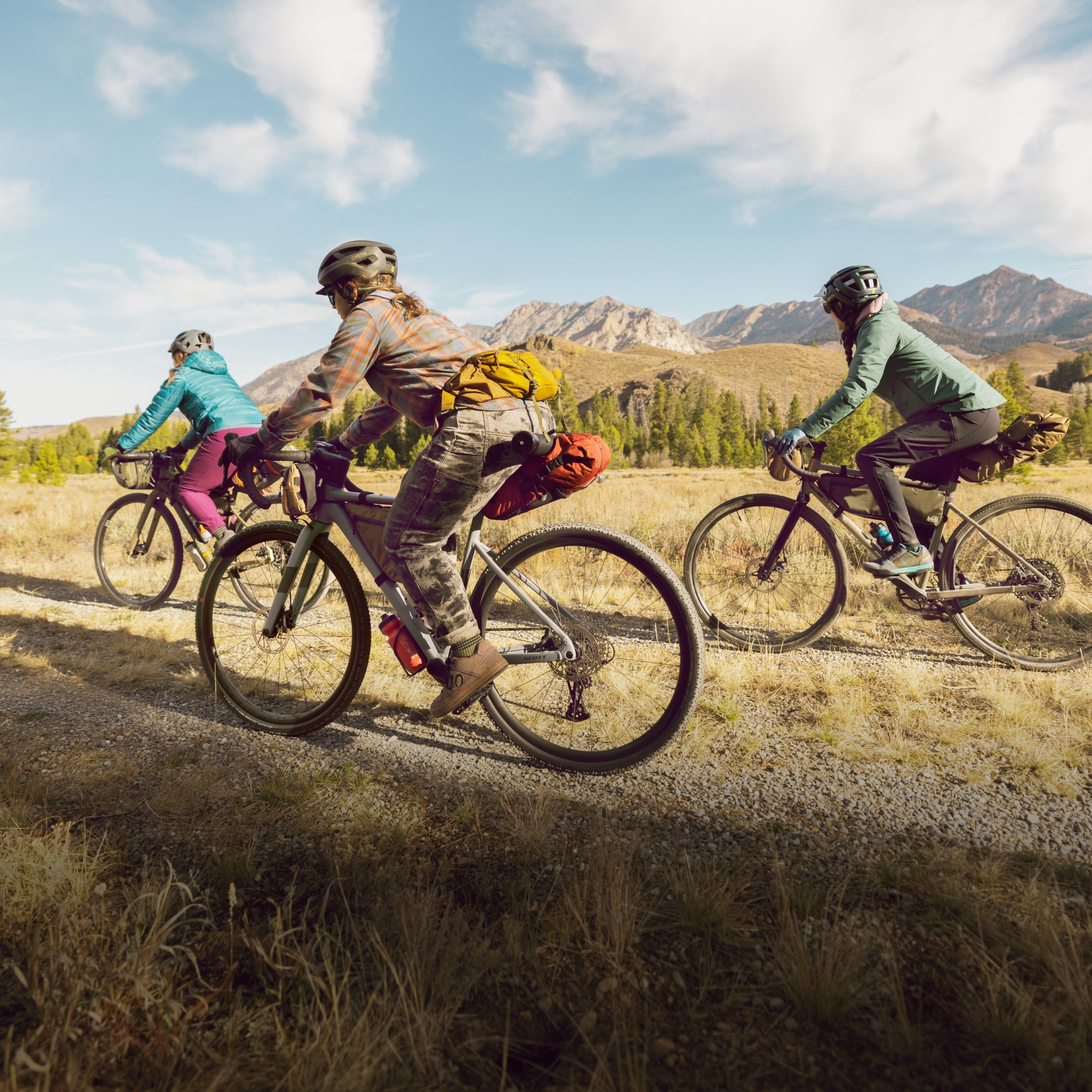 Three people ride bikes together through a gravel path on a sunny day.