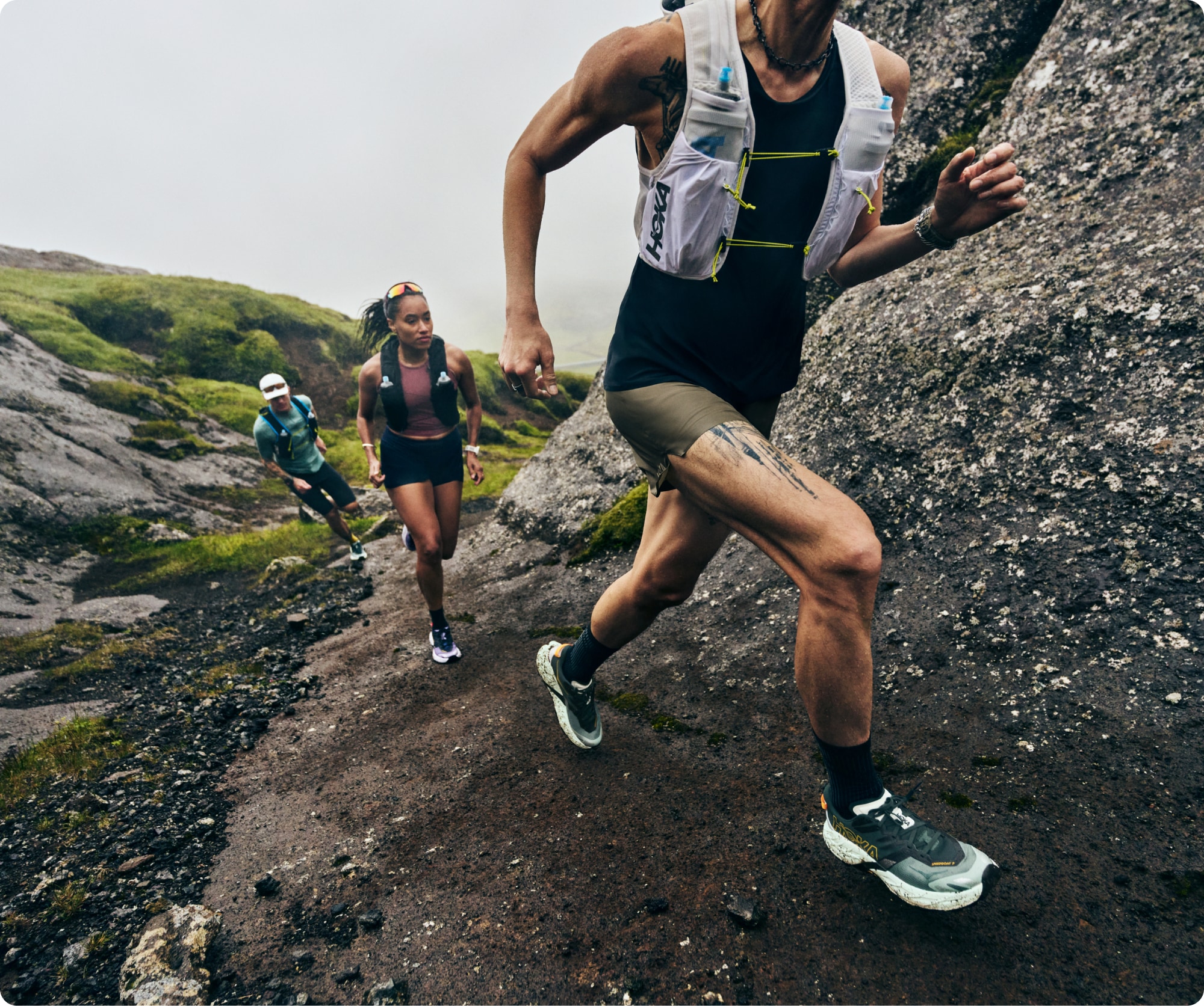 Three people run up a rocky trail in their HOKA Speedgoat 7 shoes.