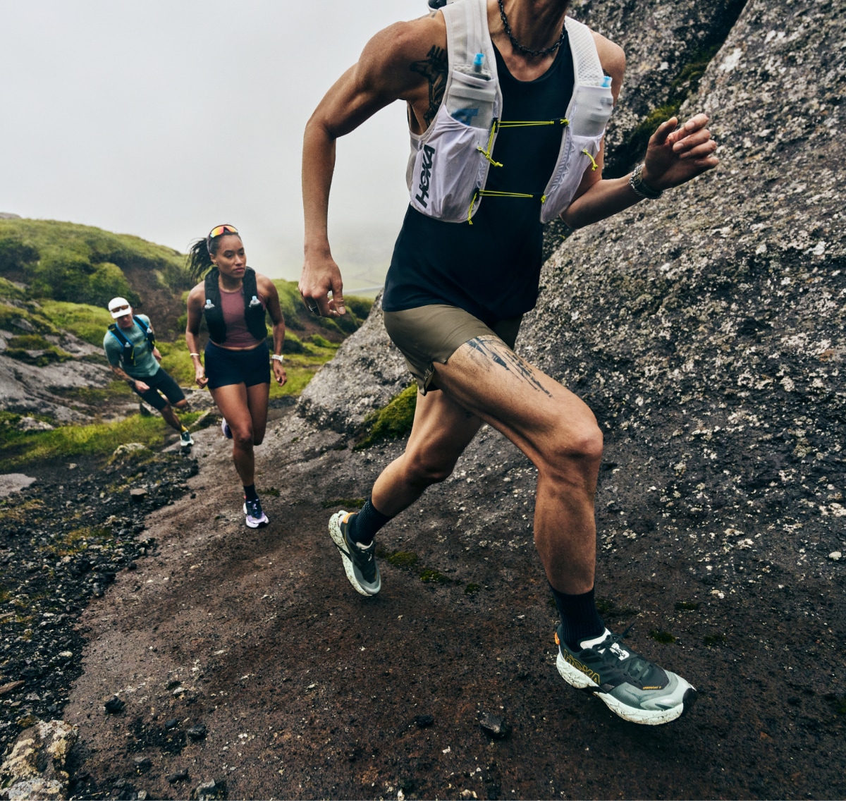 Three people run up a rocky trail in their HOKA Speedgoat 7 shoes.