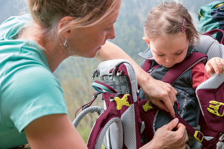A person adjusts the fit on a child carrier with a child inside