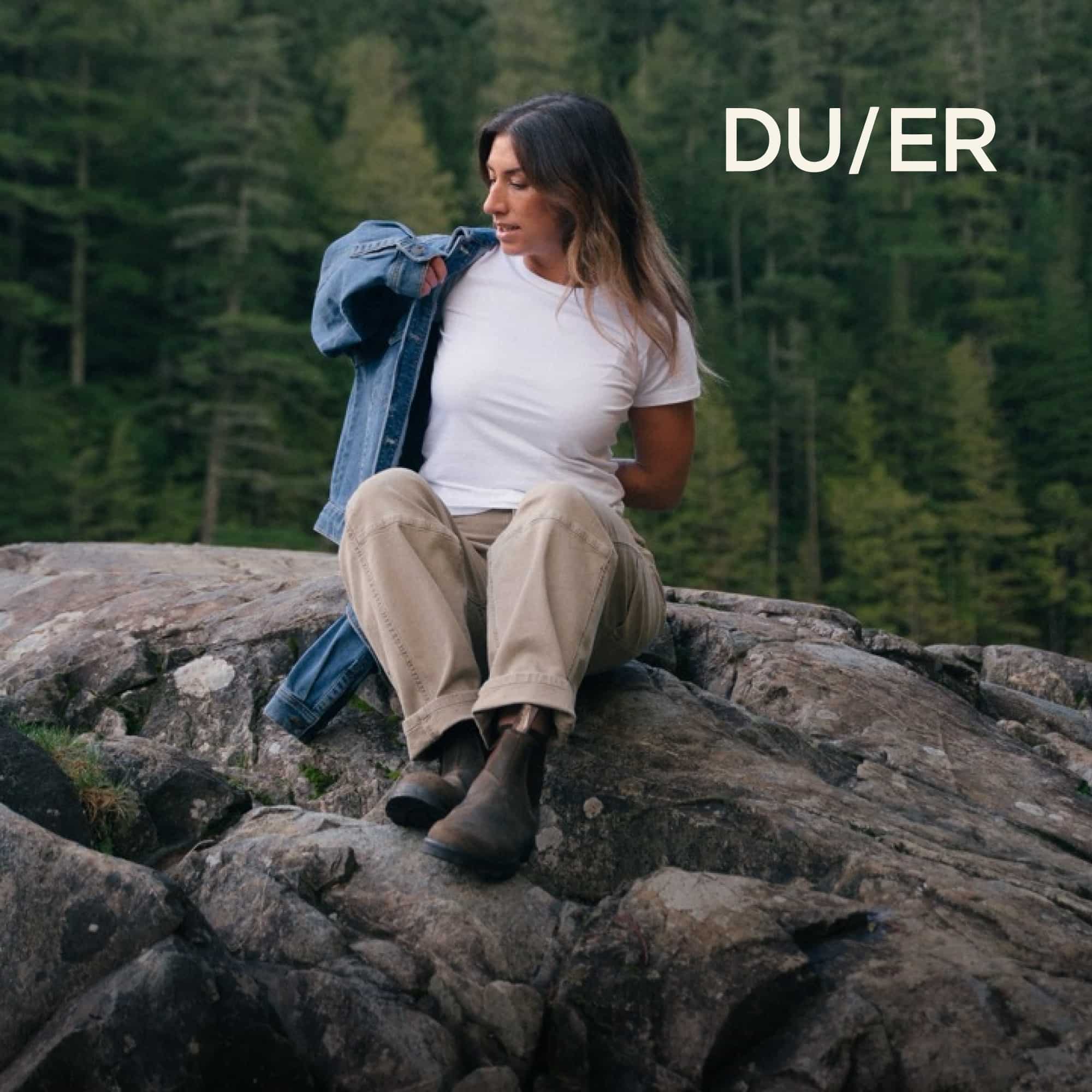 A person sits on top of a large rock in their DUER clothing.