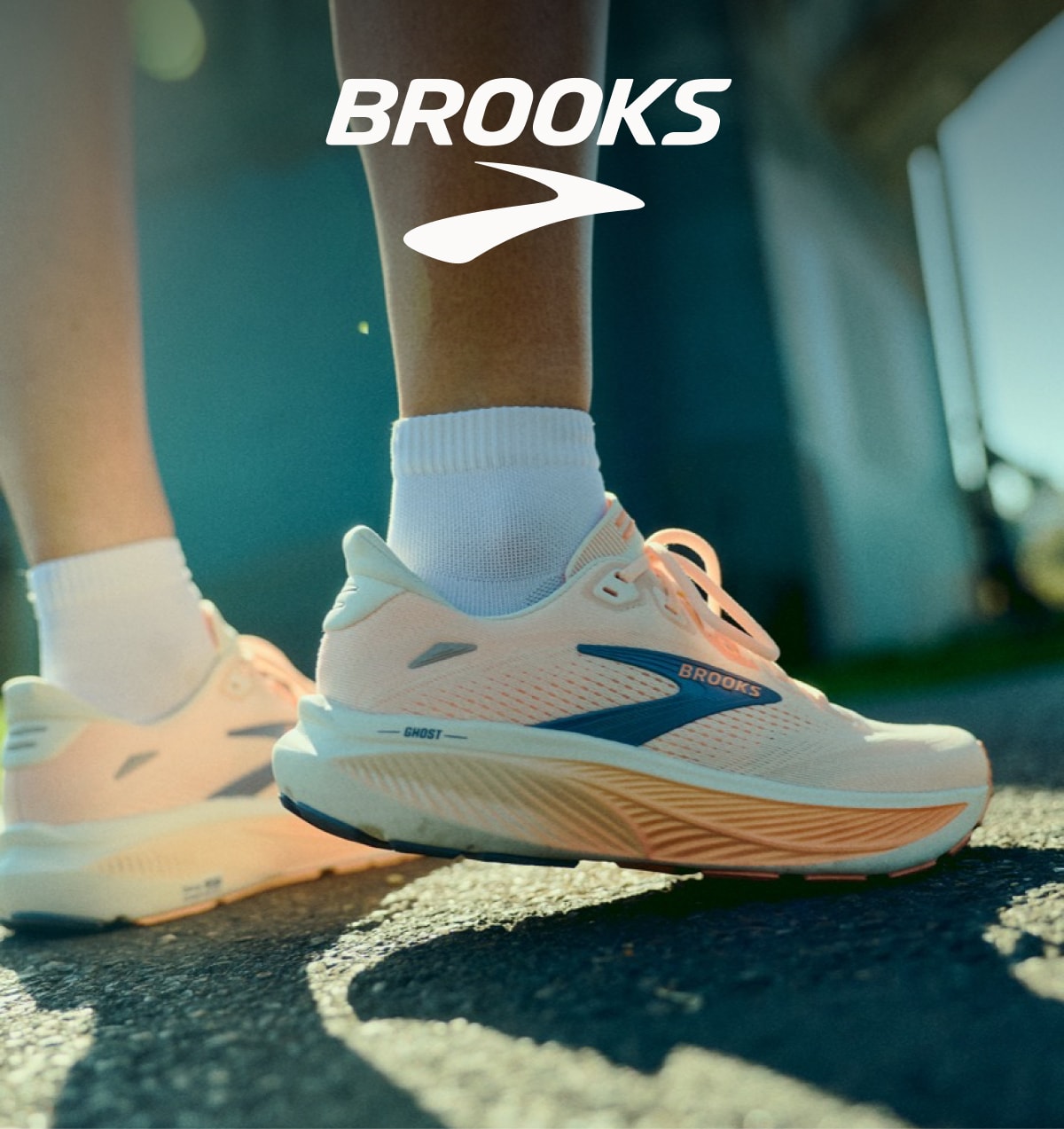 A person stands on a paved road in their Brooks Ghost 18 running shoes.