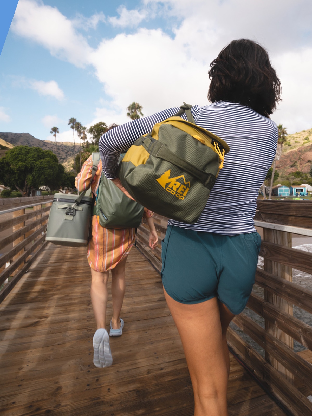 Two people walk across a wooden path with their bags.