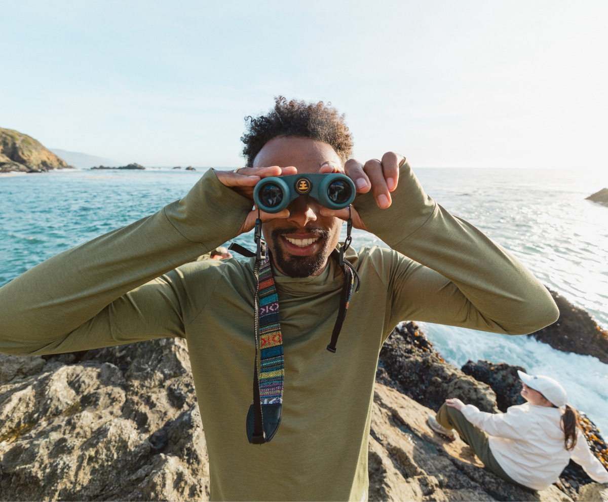 A person looks at the camera through a pair of binoculars.