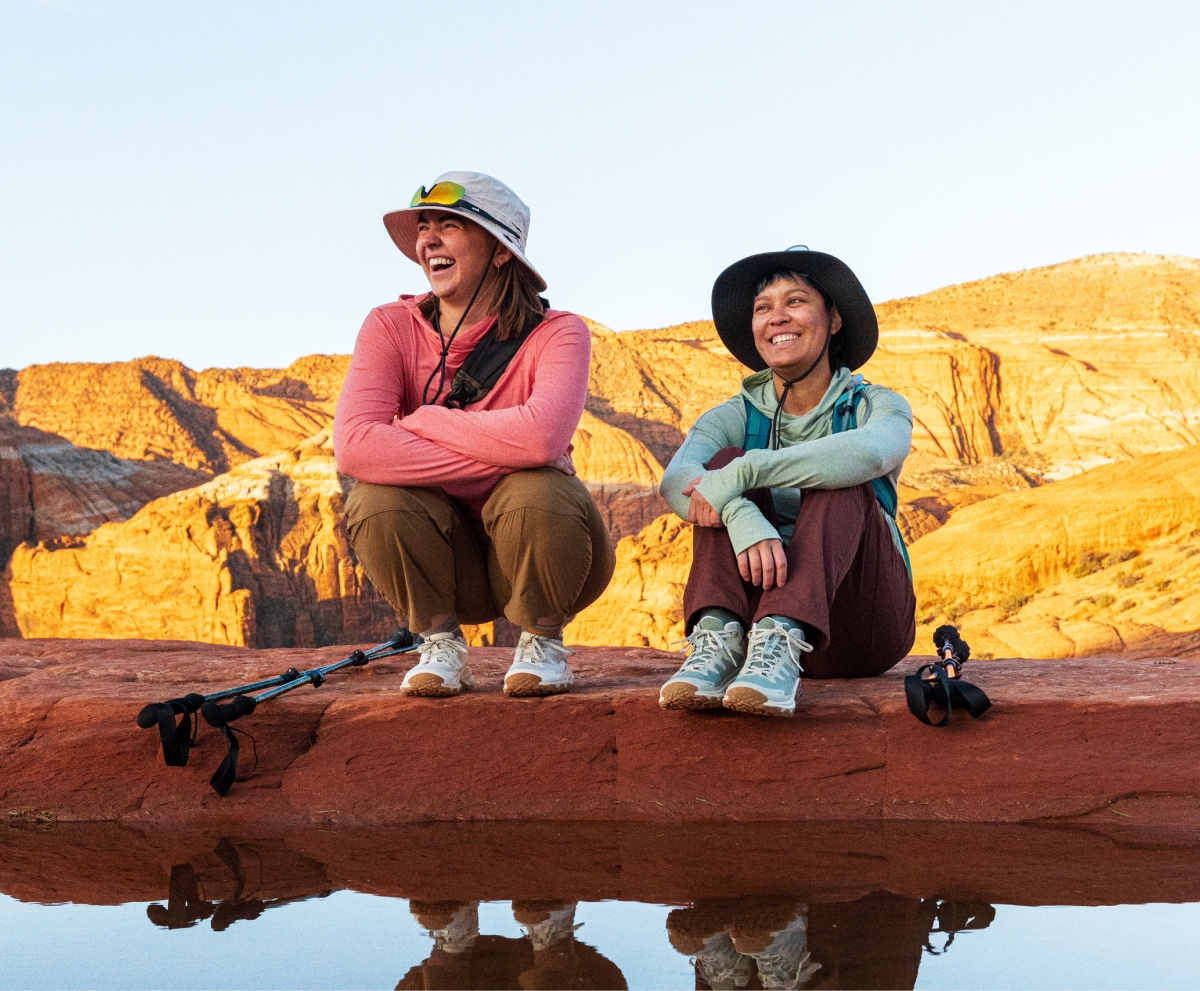 Two hikers stop to take a break and sit down while smiling for the camera.