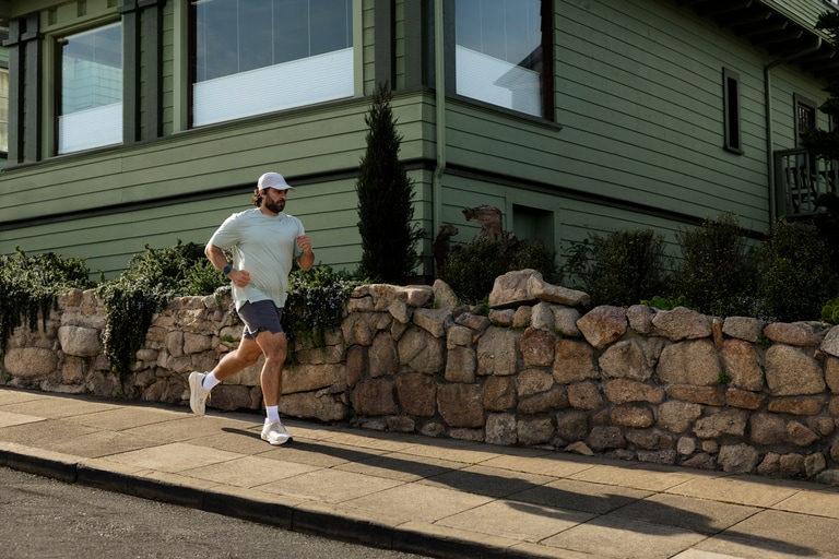 A person wearing the Garmin Forerunner 170 watch runs on sidewalk.