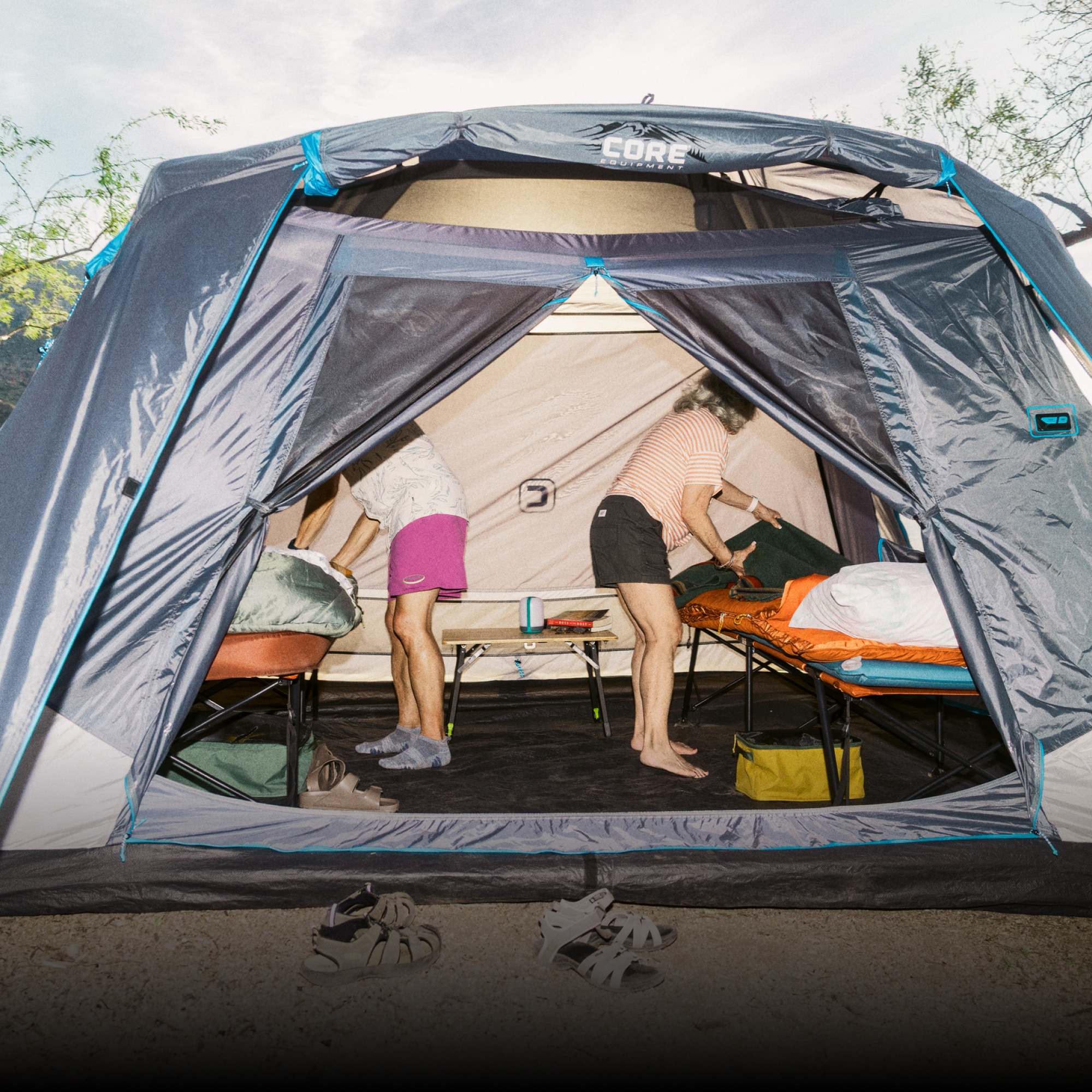 R E I Co-op & CORE Equipment. Two people fix their cots inside of a large tent.