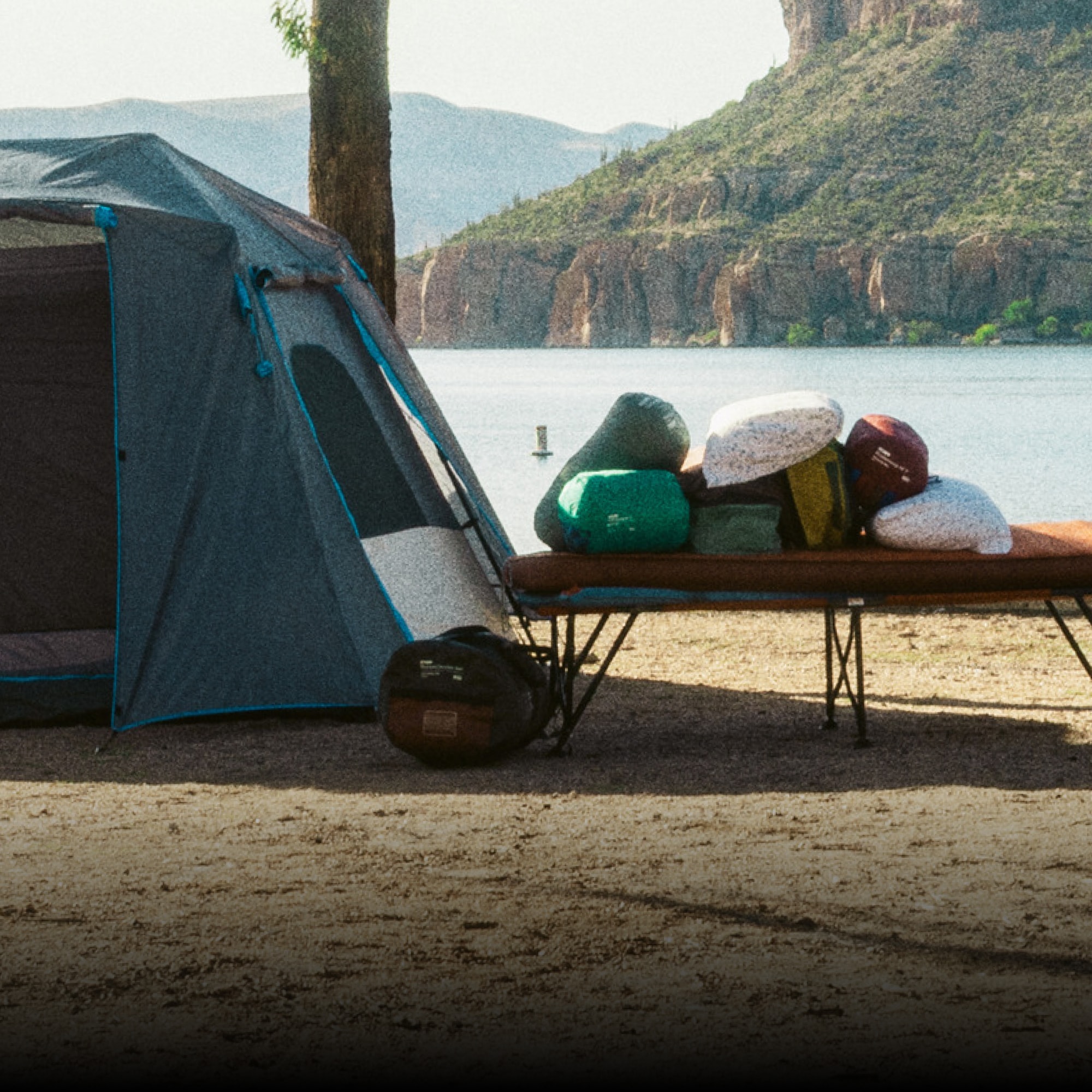 R E I Co-op, HEST, & Kelty. Sleeping bags and pillows piled on top of a cot with a tent sitting to the left of it.