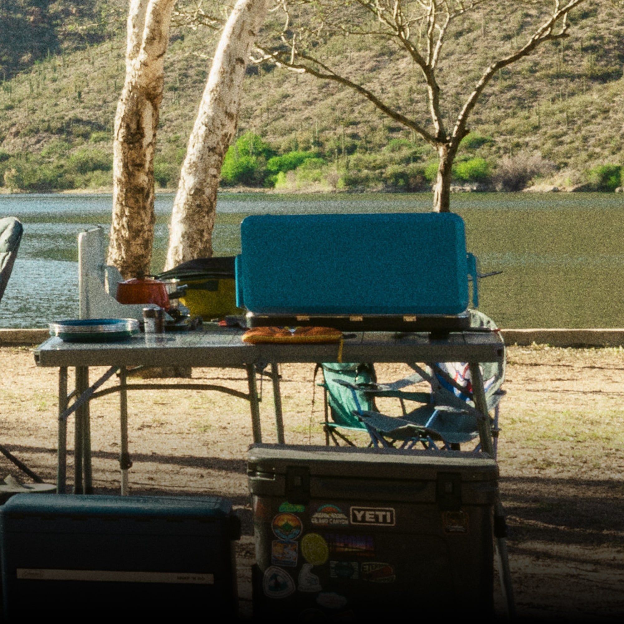 YETI & Coleman. Two coolers, a table, a portable stove, and other cooking gear.
