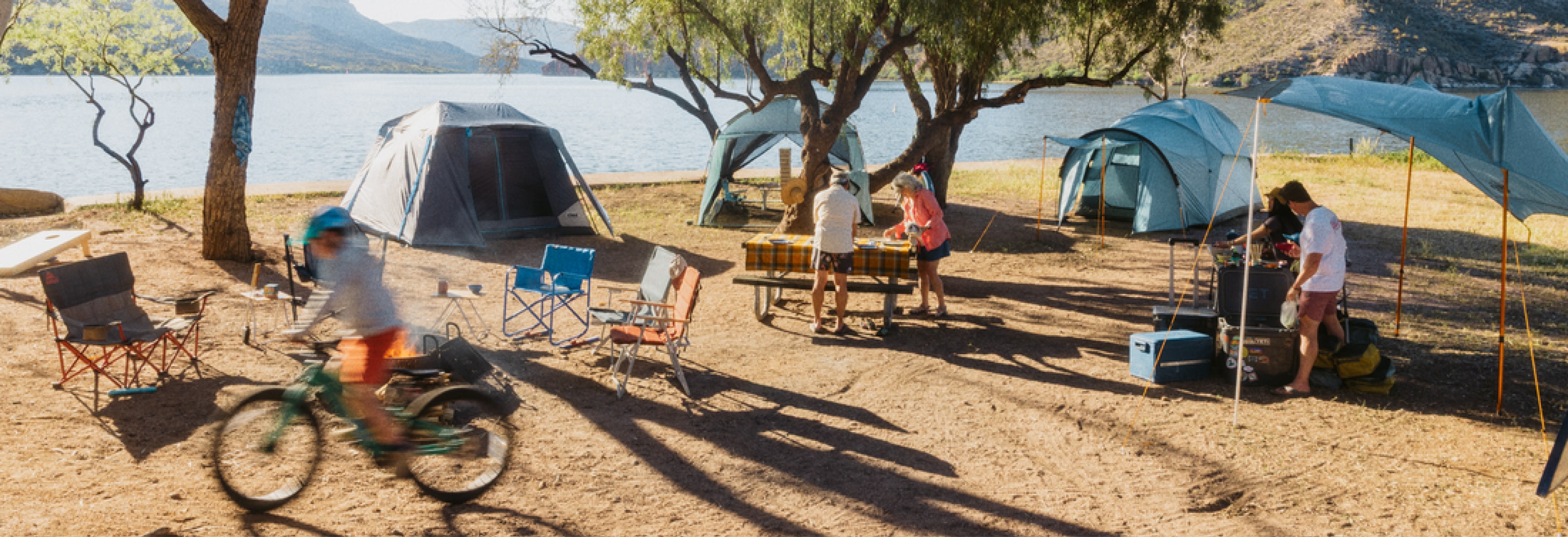 A group of people work on setting up their campsite with tents, tables, chairs & cooking gear.
