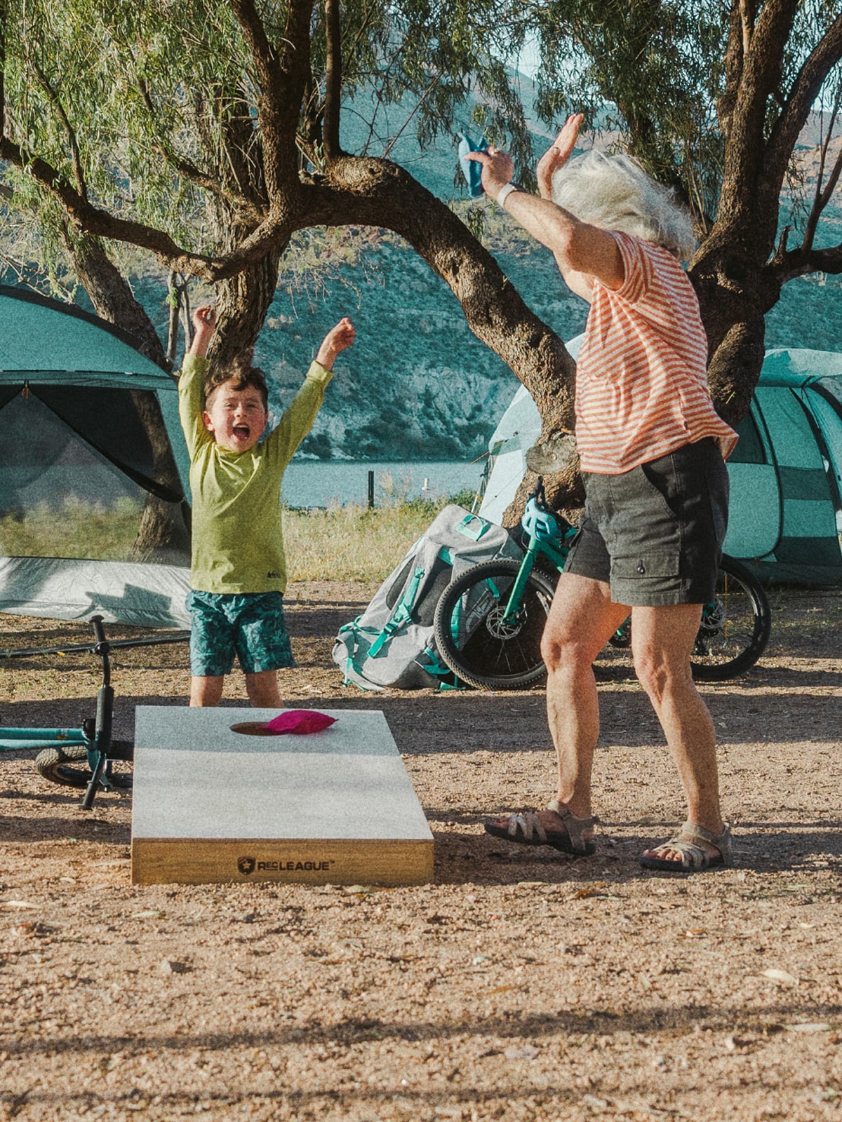 Two people laugh and cheer while playing cornhole.