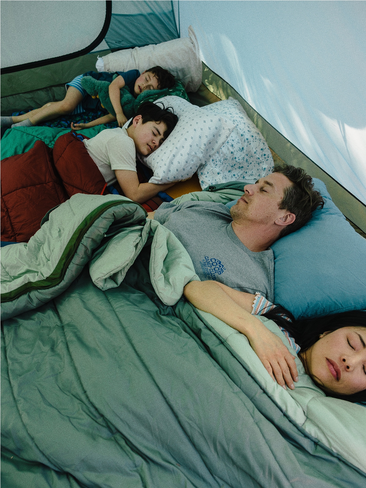 Three people sleeping inside of a tent.