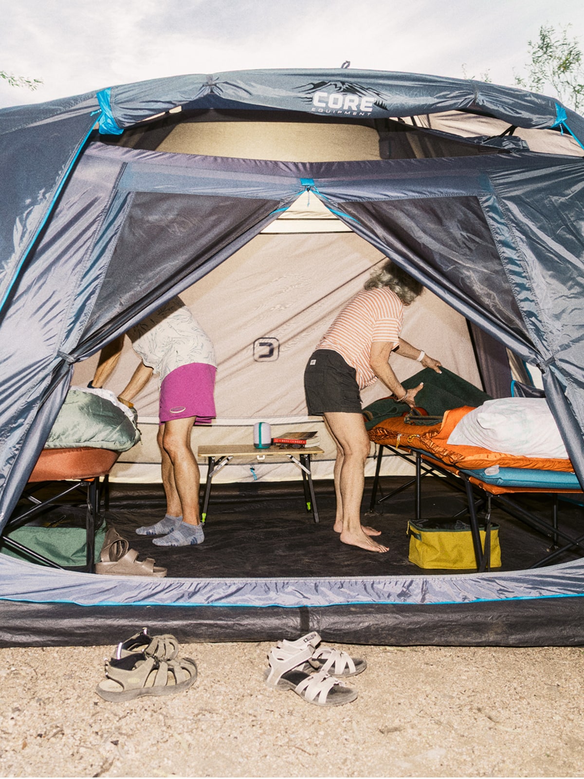 Two people fix their cots inside of a large tent.