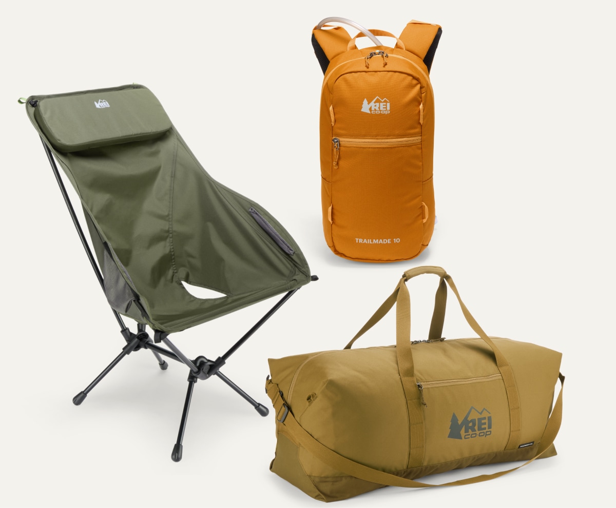 An R E I Co-op brand backpack, camp chair, and duffel bag on a light colored background.