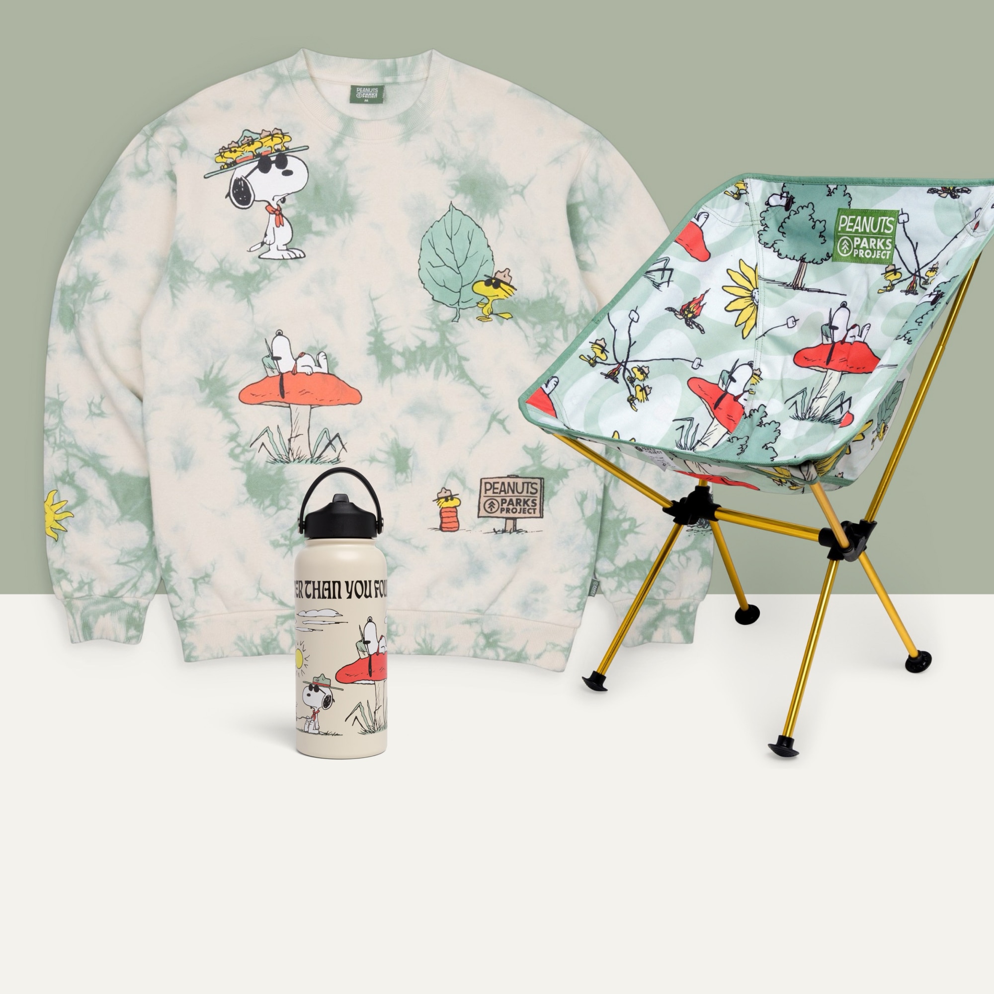 A water bottle, a sweatshirt, and a packable camp chair from the Peanuts x Parks Project collaboration on a green and white background.