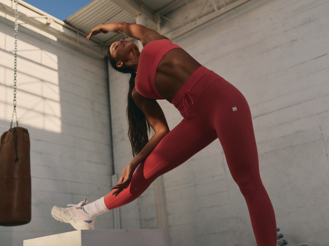 A person stretches before a workout in their Vuori top and matching leggings.