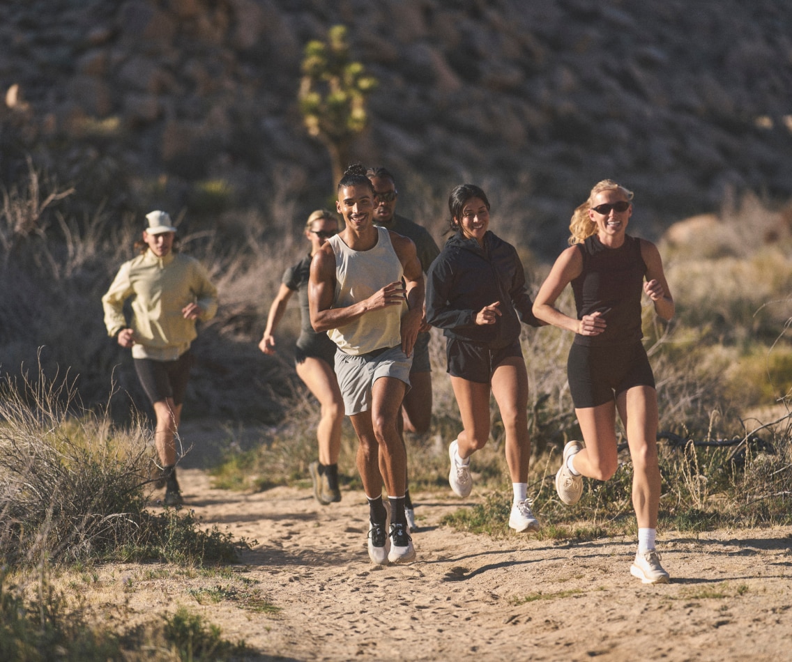 A group of people run through a desert trail together on a sunny day.